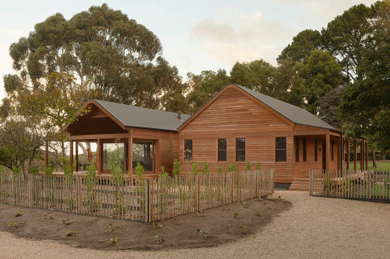 Timber-clad residence with gabled roofs and slatted fence enclosure surrounded by eucalyptus trees at dusk