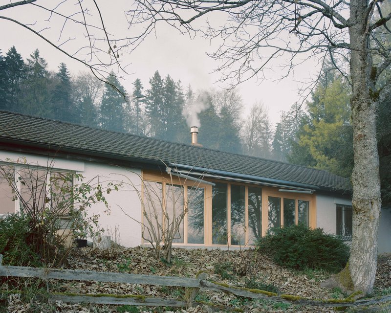 Exterior view of the low-pitched roof with chimney smoke rising into the forest mist