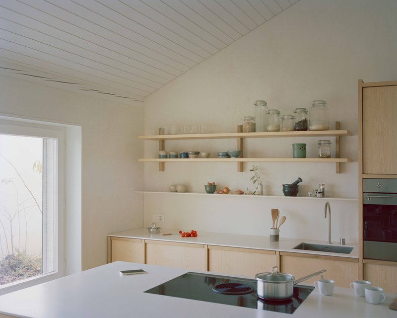 Kitchen counter with island cooktop and open timber shelving under a sloped white plank ceiling