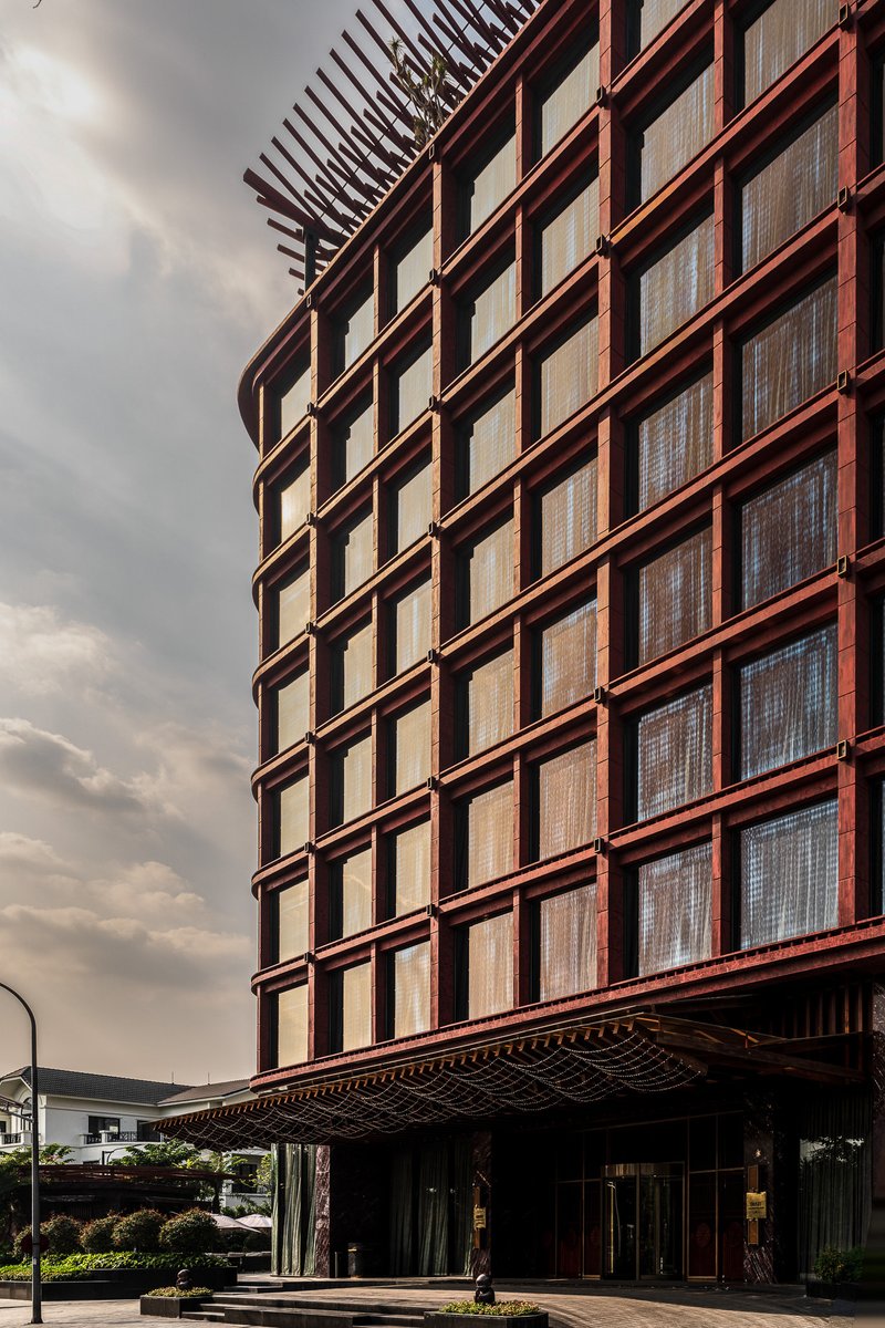 Red metal grid facade wrapping the curved corner above a canopied entrance under cloudy skies