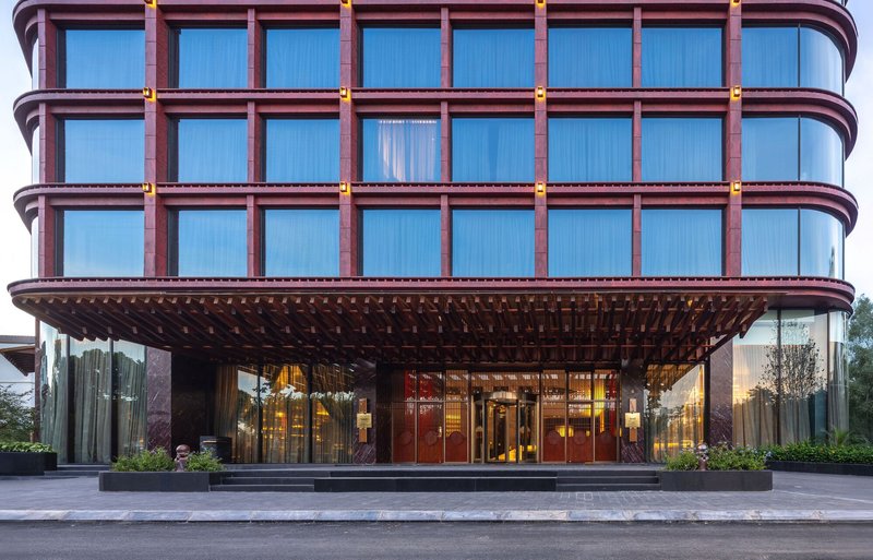 Entry canopy with rounded facade of bronze-framed windows above a covered porte-cochère at dusk
