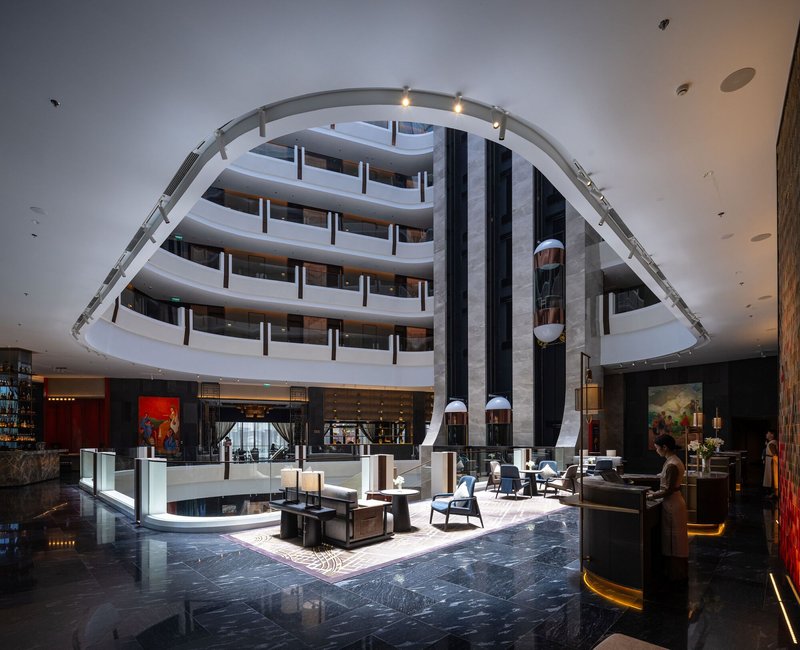 Central atrium with curved balconies rising around a skylit void and polished stone floor below