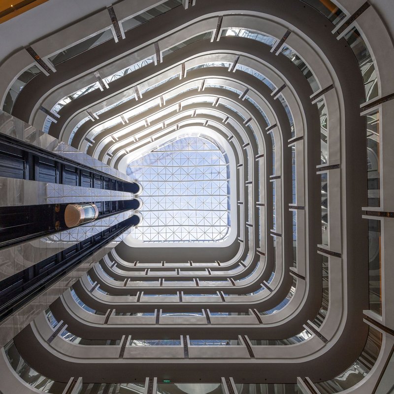 View up through the rounded atrium shaft with stacked balconies framing a glazed ceiling