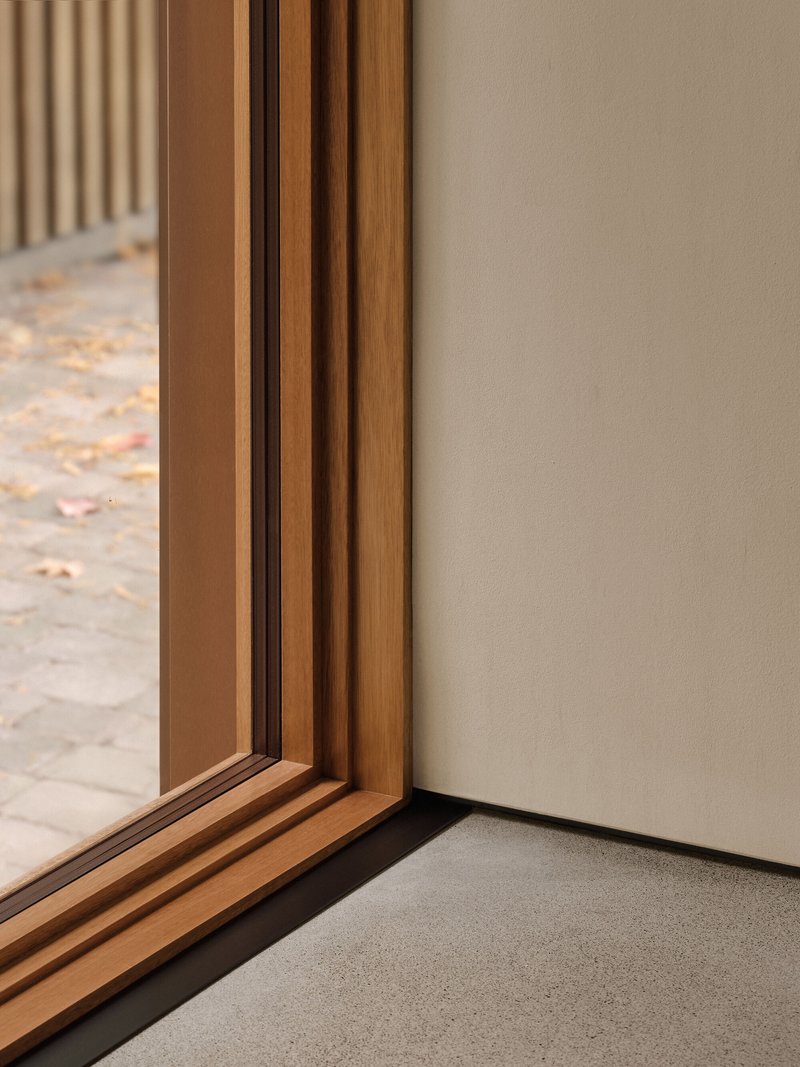 Detail of timber window frame meeting plastered wall corner with autumn leaves visible outside