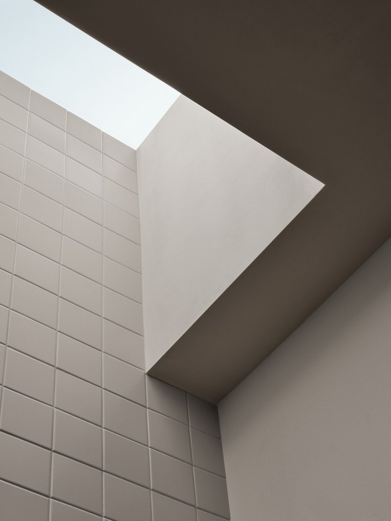 Upward view of a skylight between white tiled wall and angled plaster ceiling planes