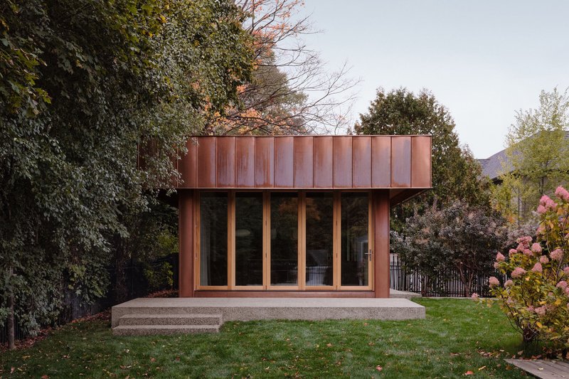 Garden pavilion with vertical copper cladding and concrete plinth surrounded by lawn and flowering shrubs