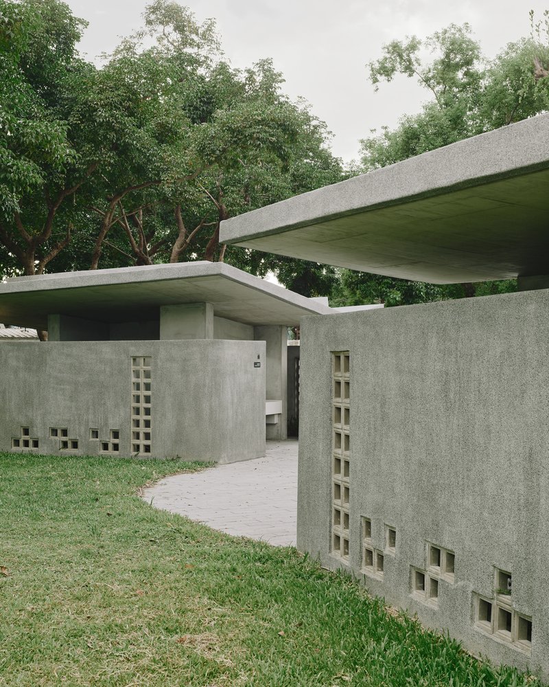 Curved brick pathway leading between concrete walls with staggered square openings and overhanging roofs
