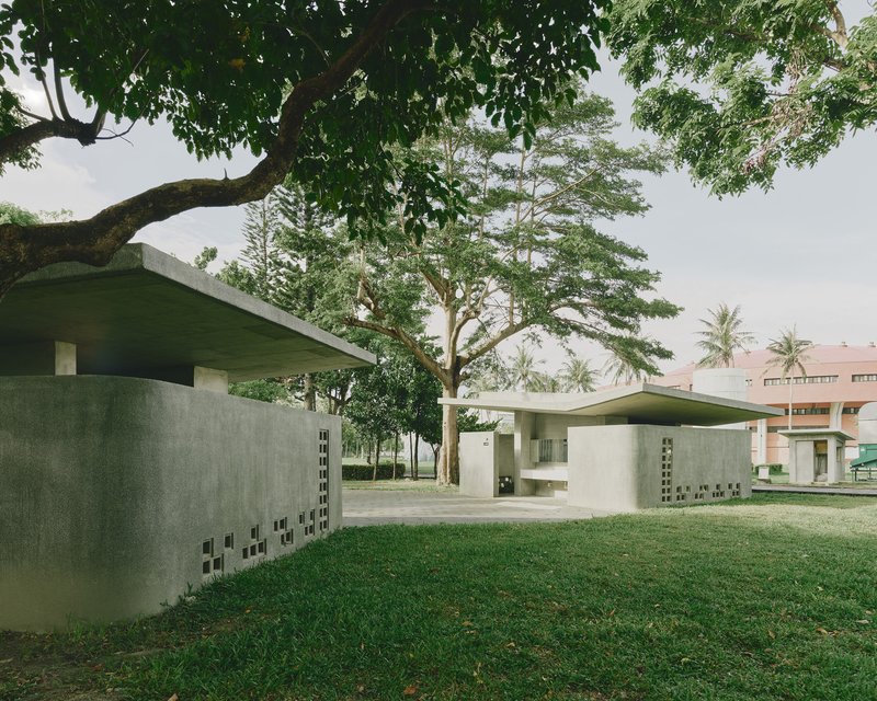 View across lawn showing curved concrete walls with geometric openings under green cantilevered roofs