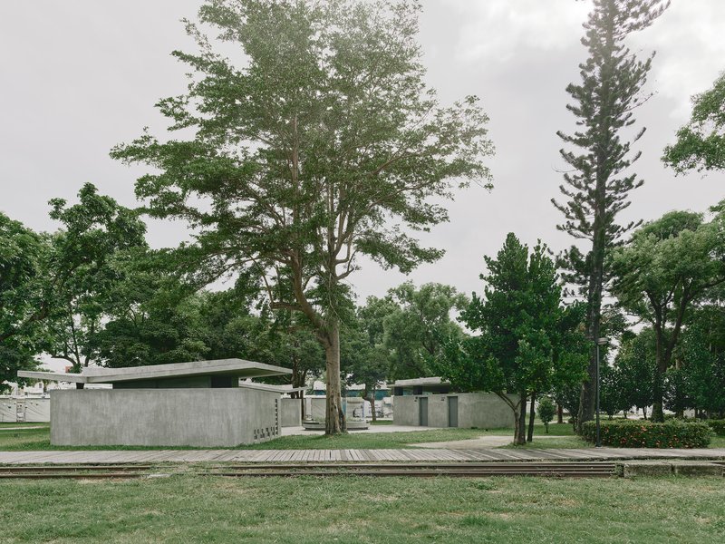 Low pavilion structures with board-formed concrete walls and thin roof planes among scattered trees
