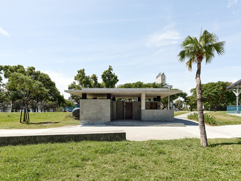 Front view of the concrete pavilion with flat roof surrounded by lawn and palm trees