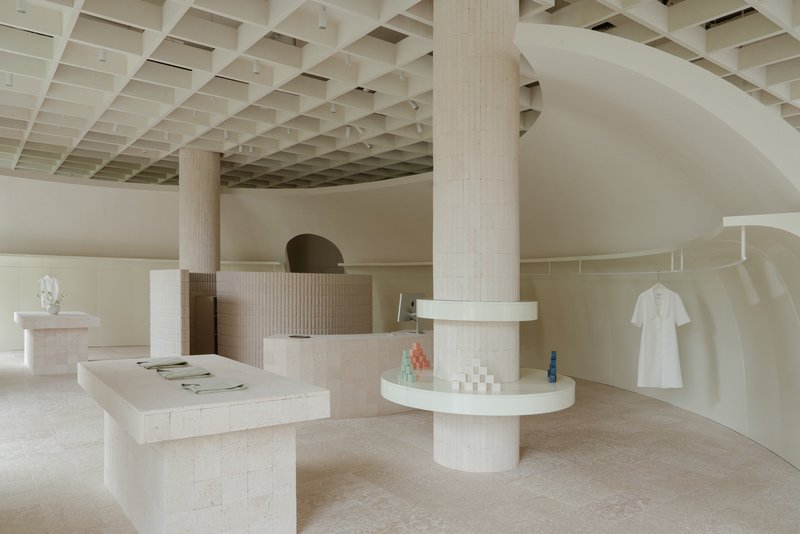 Interior retail space with coffered timber ceiling, fluted columns, and curved display walls in pale plaster