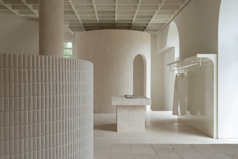 View through arched openings showing fluted cylindrical volume and stone display plinths under gridded ceiling