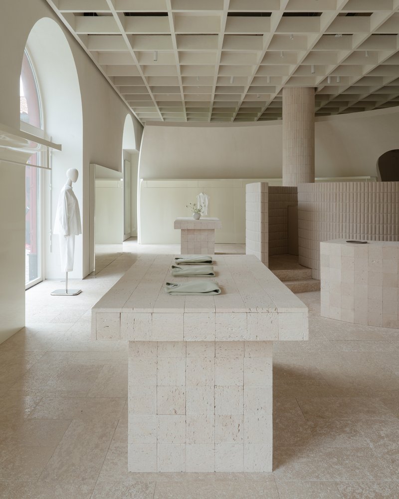 Long stone display table with arched windows and mannequin under exposed timber coffered ceiling