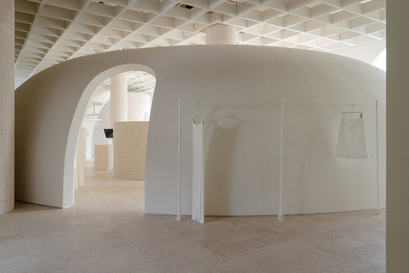 Curved wall with arched openings and hanging garments displayed on freestanding panels