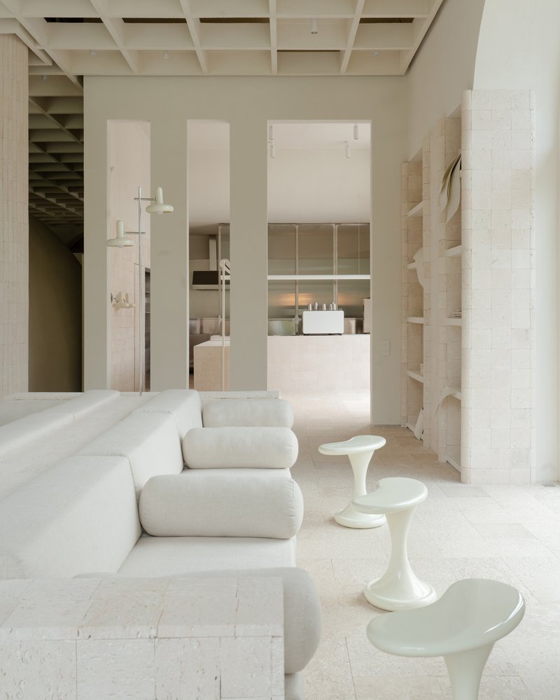 Open plan living space with pale upholstered seating and sculptural side tables under gridded ceiling