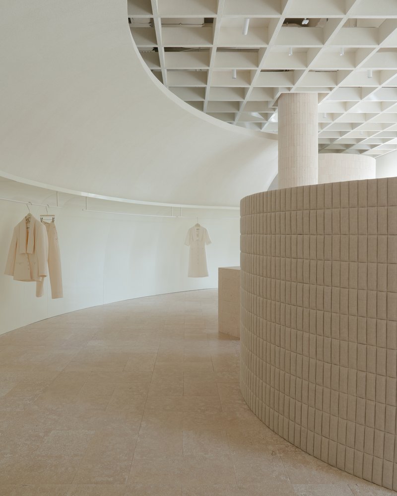 Curved retail wall clad in ribbed timber tiles beneath a coffered ceiling with garments on display