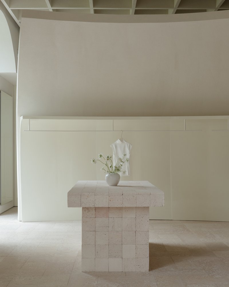 Travertine pedestal table with a vase of white flowers beneath a coffered ceiling and paneled wall