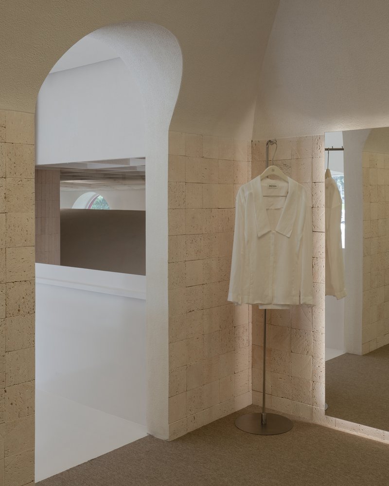 Arched window opening with horizontal timber louvers and a white garment hanging on a display stand