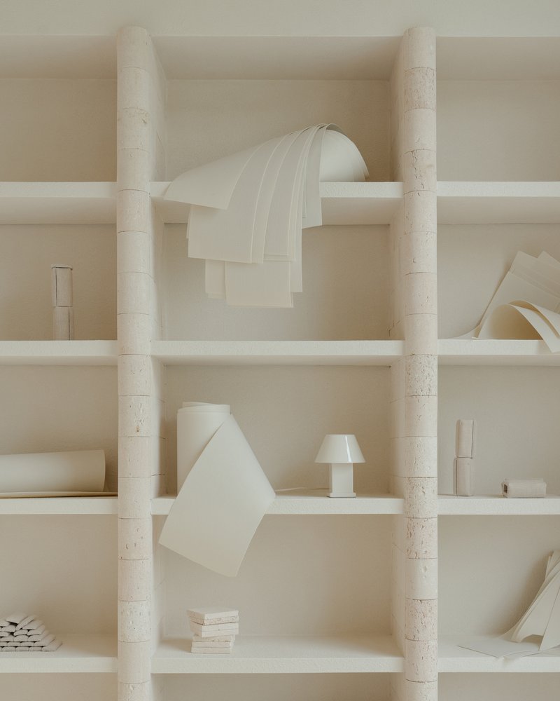 Close-up of shelving niches with cylindrical stone columns and folded paper forms in neutral tones