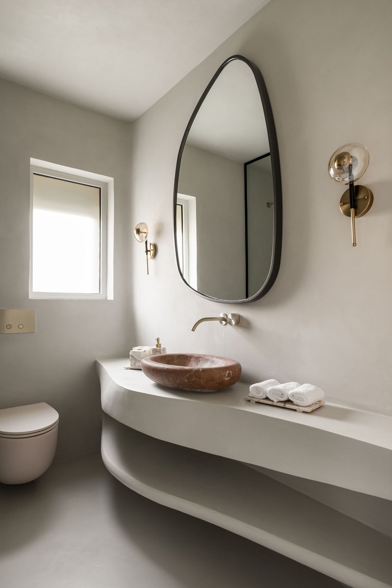 Bathroom vanity with organic mirror, copper vessel sink and brass wall-mounted faucet and sconces