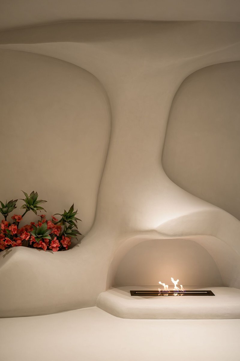 Curved plaster alcove with built-in fireplace and planted bed of flowering shrubs beneath warm ambient lighting