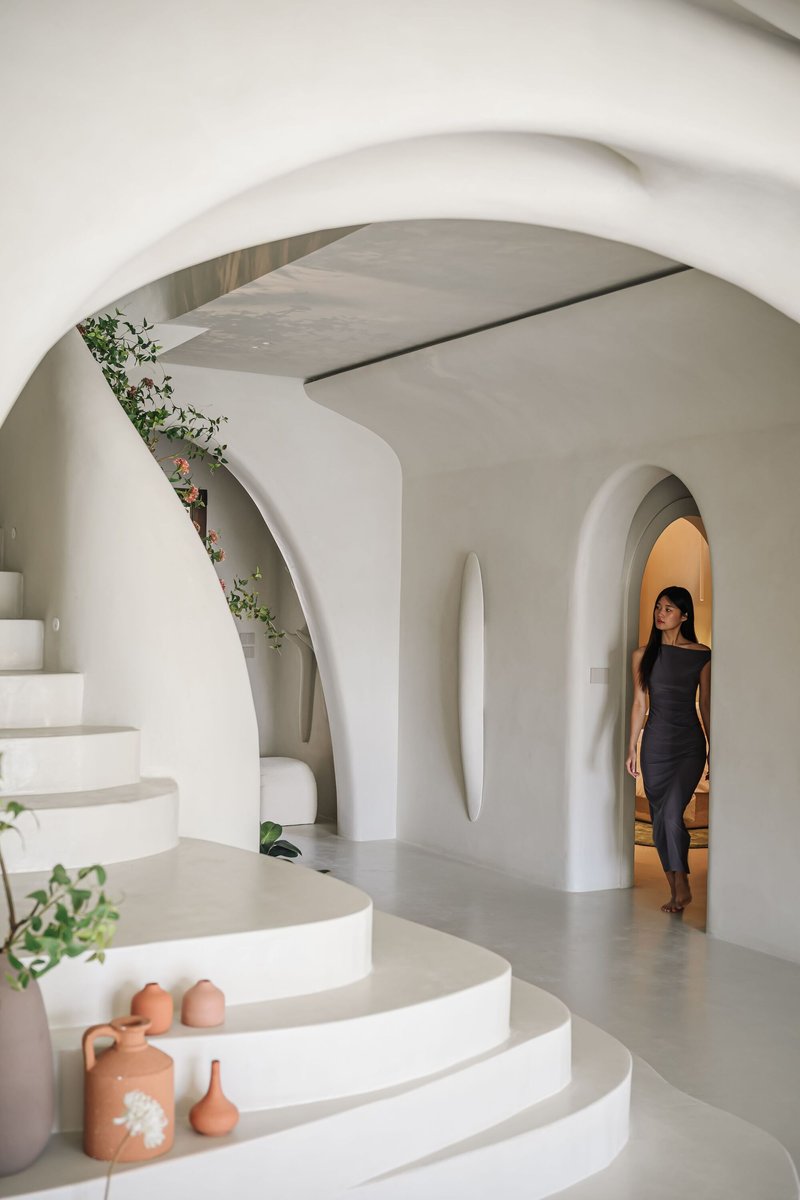 White curved staircase with integrated planters and arched doorway where a woman stands in afternoon light