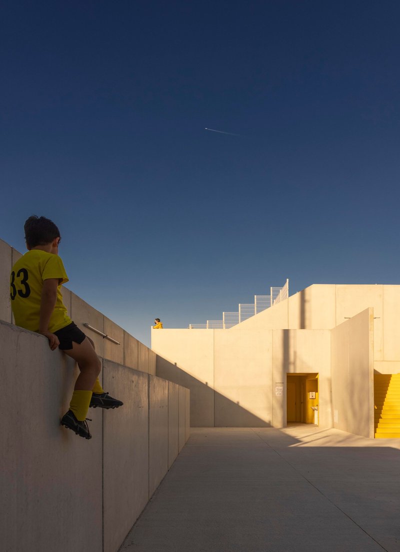 Player sitting on a boardformed concrete retaining wall beside a stucco entry passage at dusk