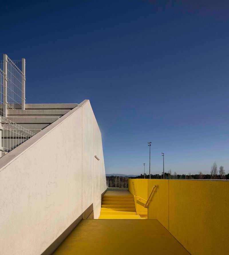 Yellow stairwell descending between white concrete walls under a clear blue sky
