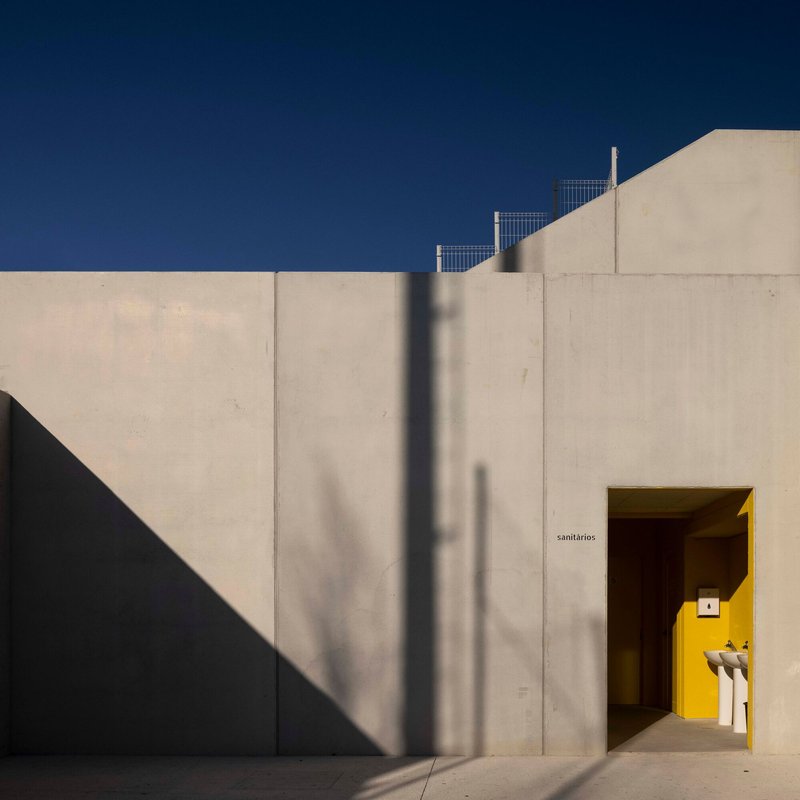 Concrete courtyard wall with yellow-framed entry portal casting diagonal shadows under clear blue sky