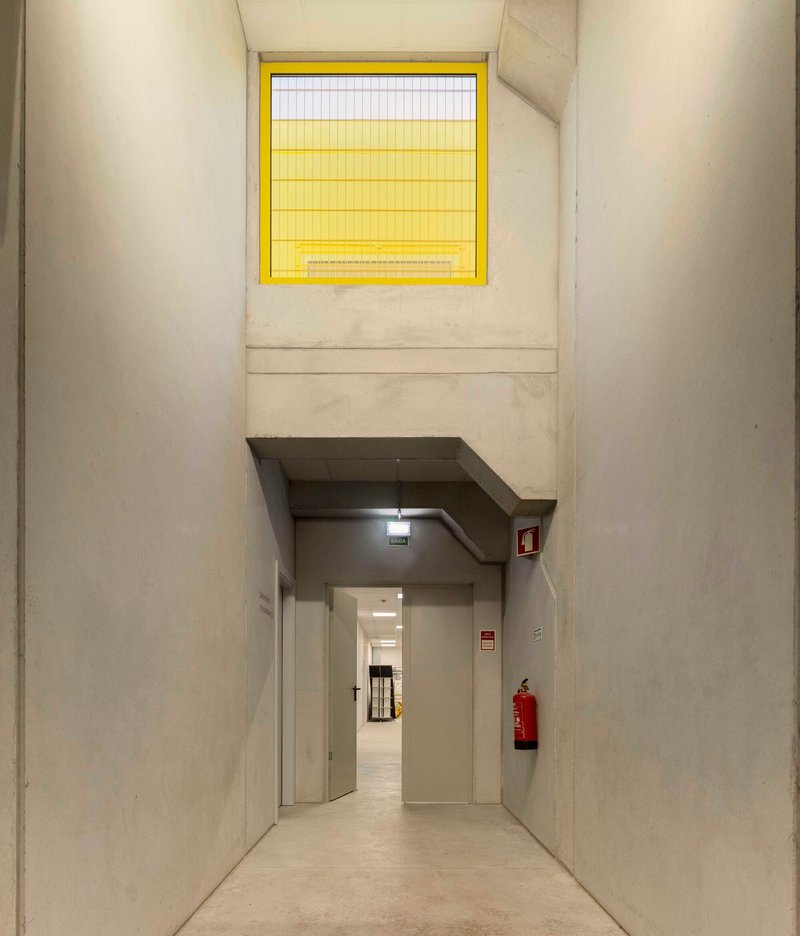 Double-height interior passage with yellow wire glass window above doorway in cast concrete walls