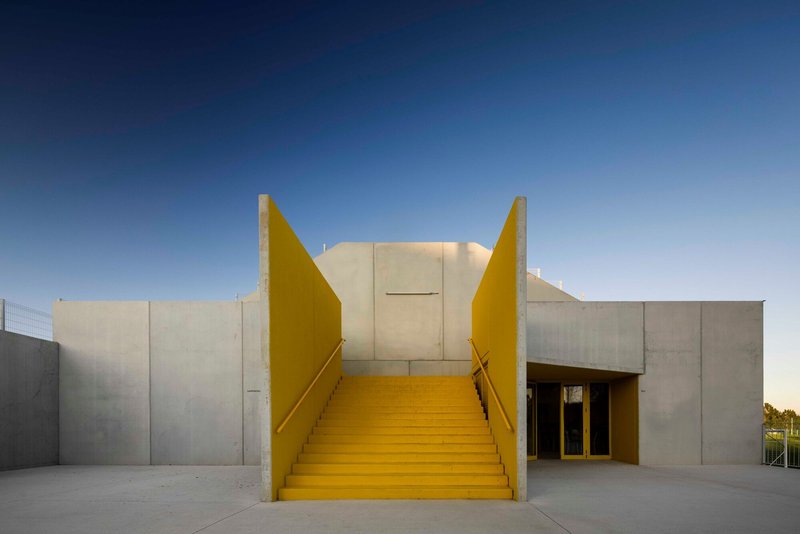 Frontal view of the yellow external staircase rising between symmetrical concrete walls at dusk