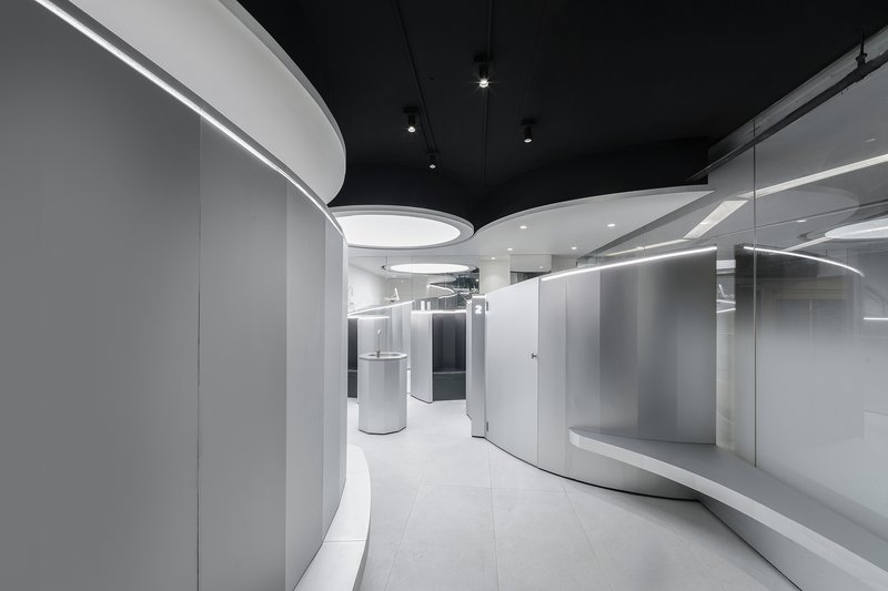 Curved white walls with integrated linear lighting beneath a black ceiling with circular recessed fixtures