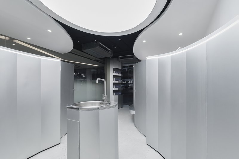 Curved white corridor with cylindrical handwashing unit and black ceiling revealing exposed mechanical systems