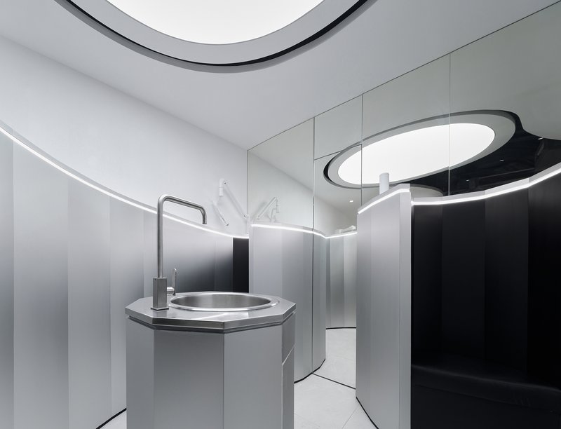 Octagonal sink with brushed metal basin and faucet beneath a curved black and white ceiling element