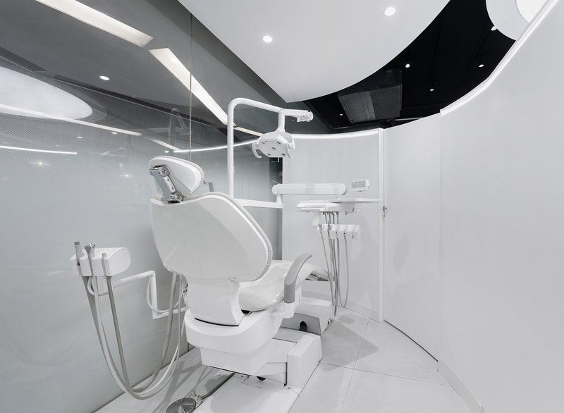 Dental chair with overhead lamp and equipment arm in a glazed treatment room with curved ceiling