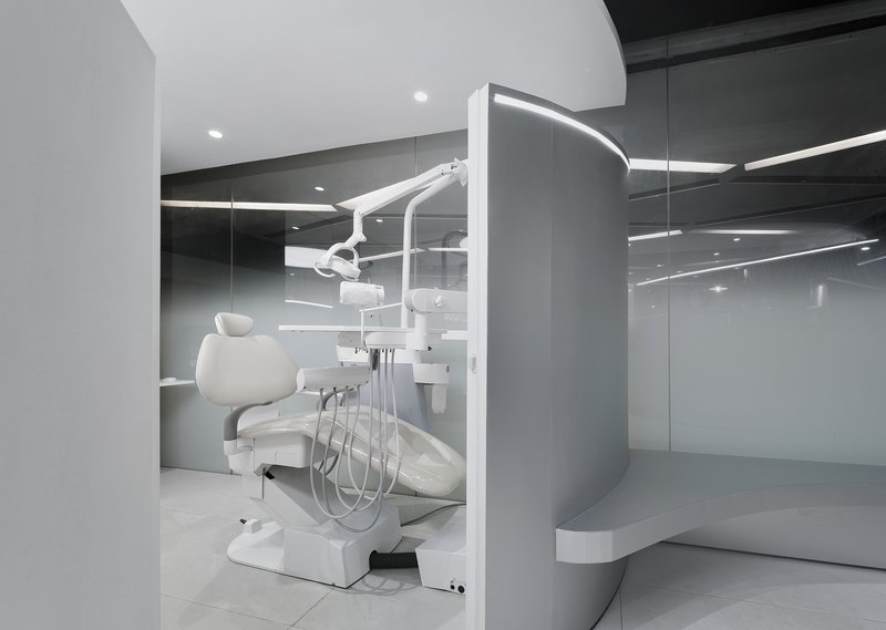 Dental treatment station with chair and articulating light within a curved partition and mirrored wall