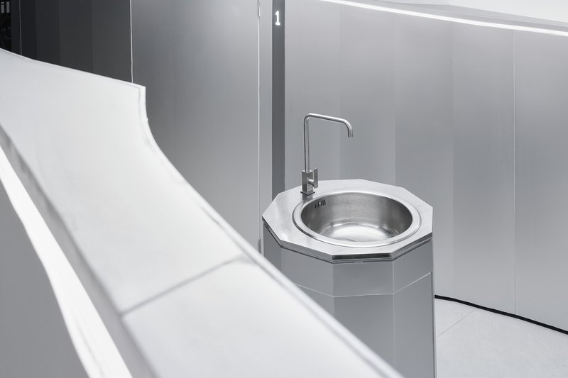 Detail of octagonal sink basin with metal bowl and tap against grey wall panels
