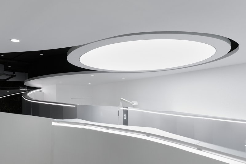 Curved reception counter with integrated LED strip lighting beneath an oval ceiling coffer with black accent