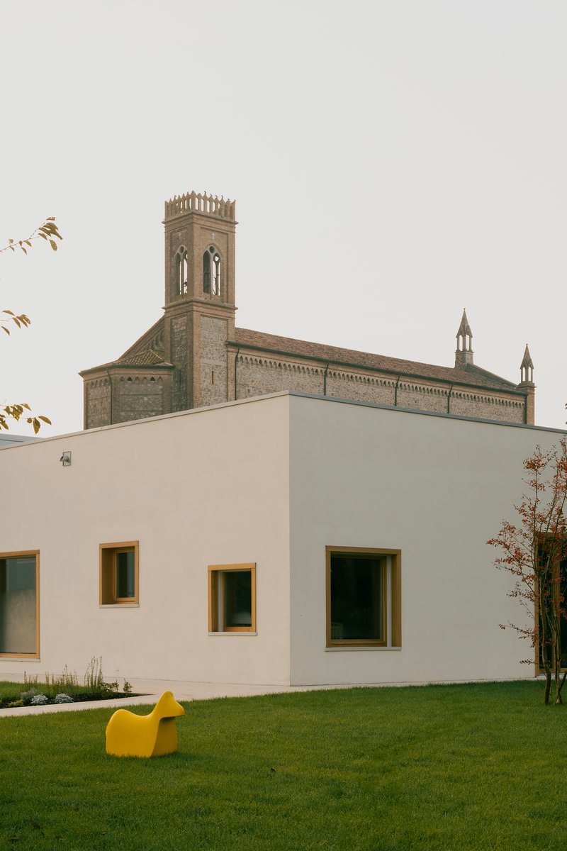 White plastered wall with timber window openings backed by a historic brick bell tower