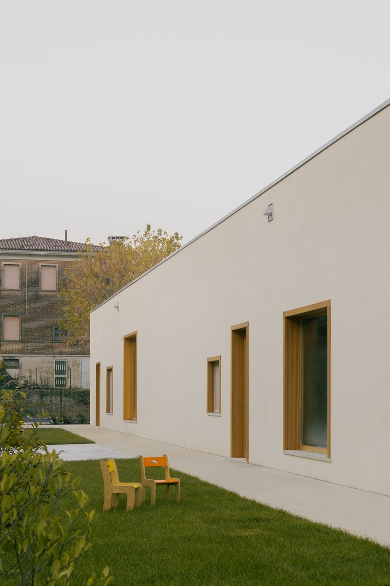 Angled stucco facade with timber-lined window reveals overlooking a courtyard with yellow furniture