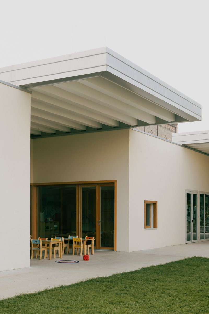 Covered outdoor terrace with exposed timber beams and wooden framed doors opening to a classroom space