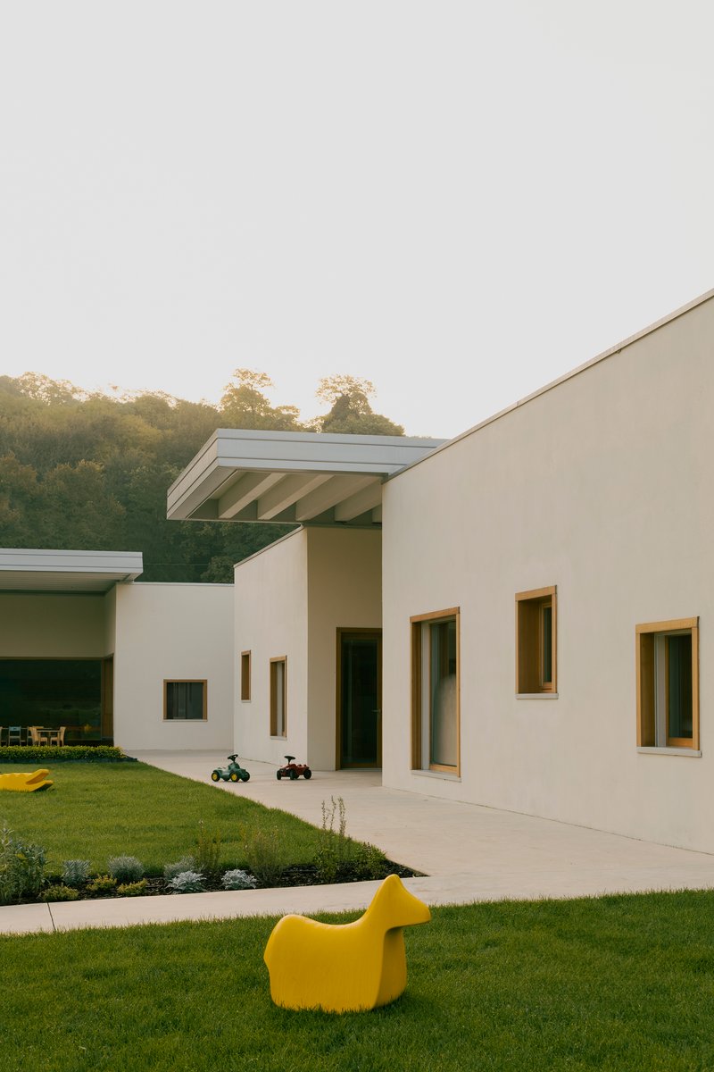 White stucco facade with timber-framed windows facing a lawn with yellow sculptural seating