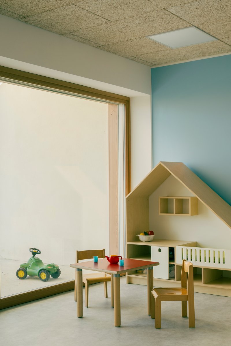 Interior playroom with house-shaped storage unit against a blue wall beneath a cork panel ceiling