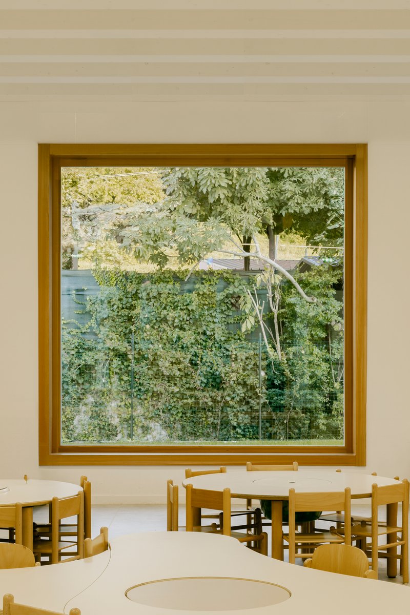 Large timber-framed window overlooking dense green foliage with children's tables and chairs in the foreground