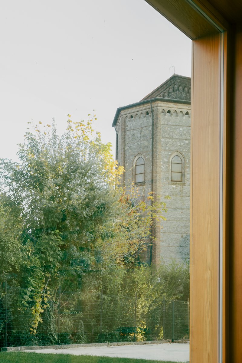 Window view framing a stone church tower through autumn trees beyond the timber frame