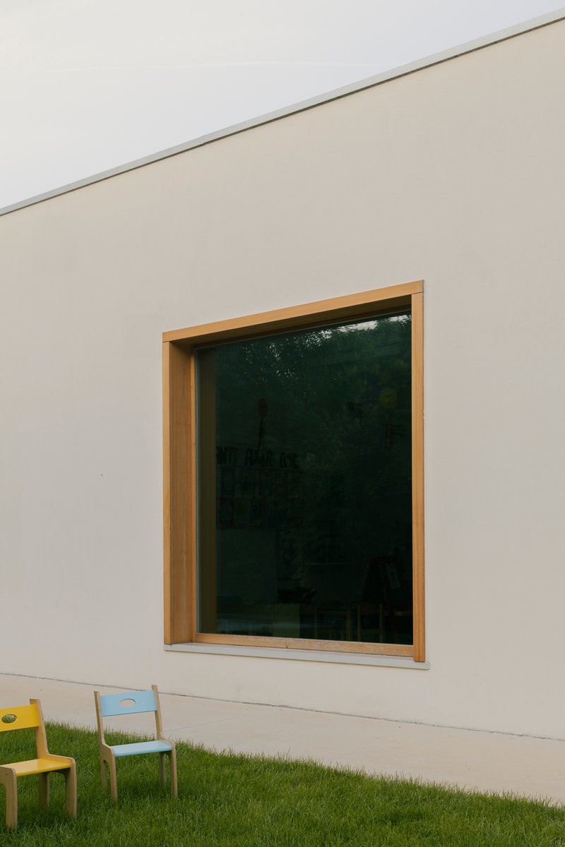 Timber-framed window set into white rendered facade with two children's chairs on grass lawn below