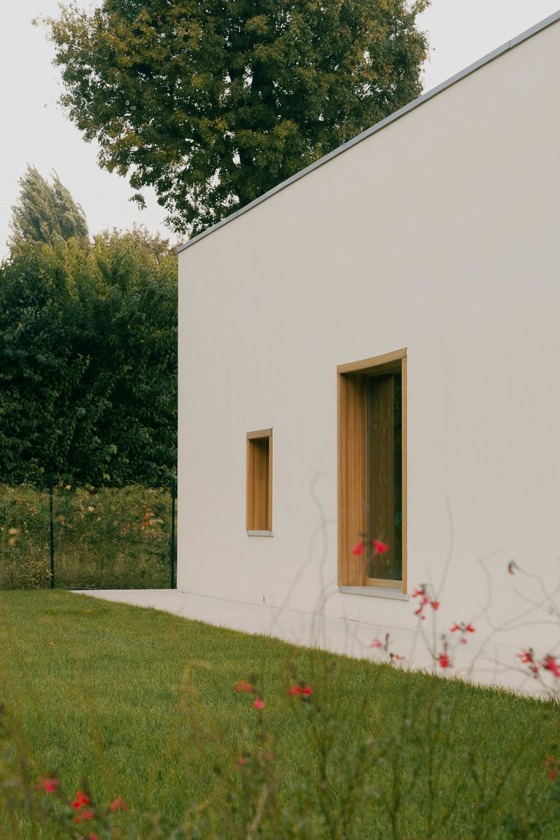 White rendered facade with timber-framed door and narrow window against green lawn with red wildflowers