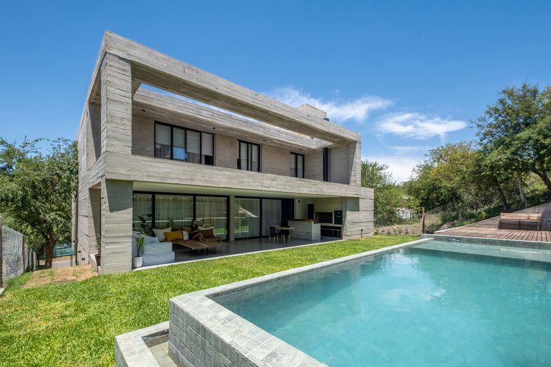 Board-formed concrete house with cantilevered upper floor overlooking a swimming pool and sloped lawn