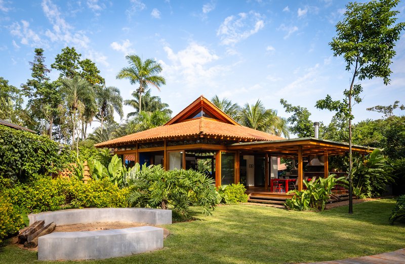 Garden view of open-sided pavilion with terracotta tile roof and concrete bench under palm trees