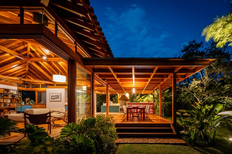 Covered terrace with exposed timber beam ceiling and glazed walls opening to dining area at night